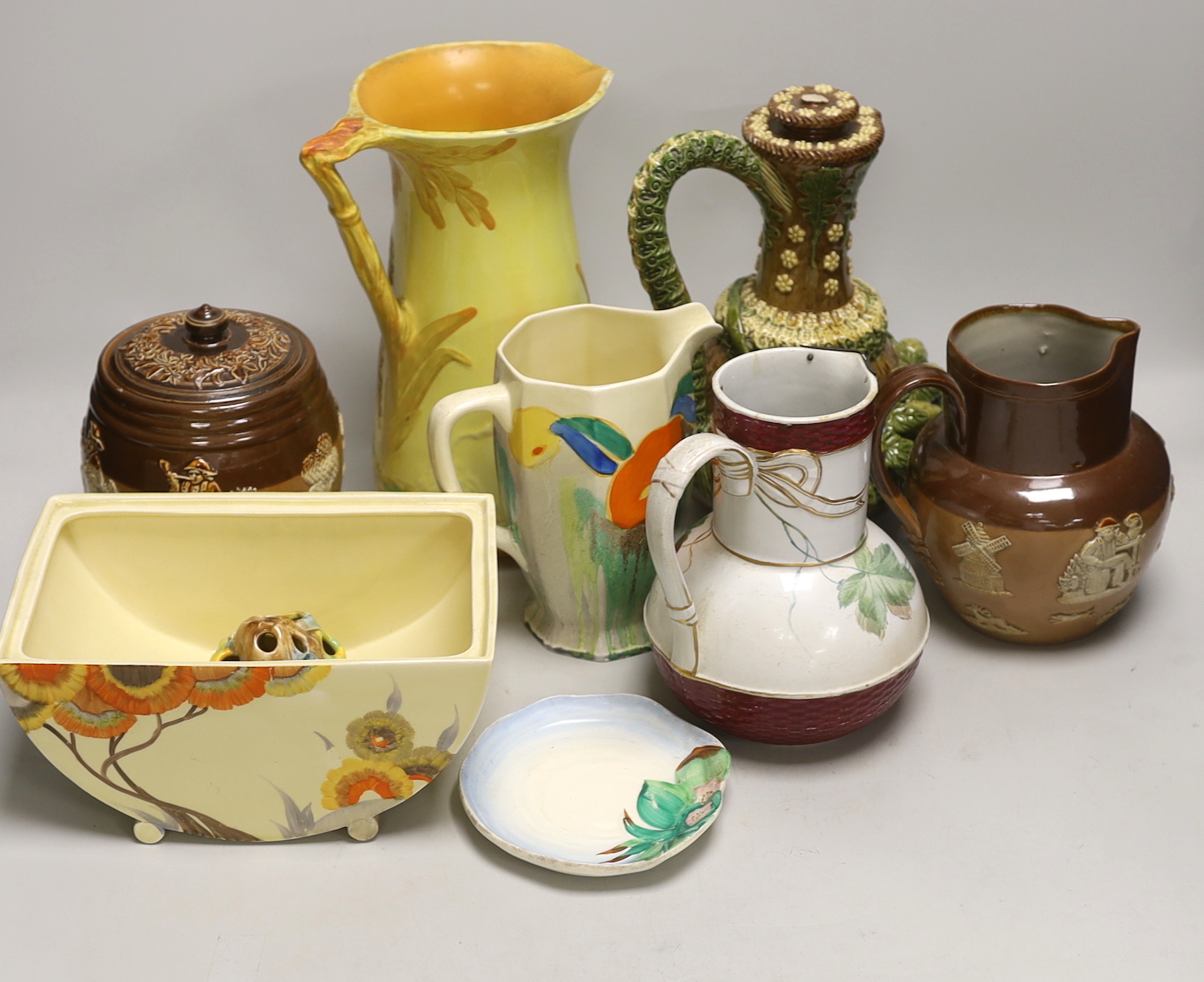 Four Clarice Cliff items; a miniature dish, jug, etc. together with four jugs and a biscuit barrel, tallest jug 24cm